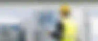 Ein Mann der einen gelben Bauhelm und eine gelbe Warnweste trägt steht vor einem Wasserstofftank